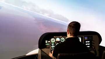 A pilot controls a flight simulator in a virtual environment.