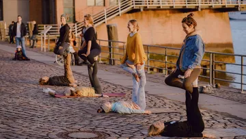 Personen stehen und liegen auf Steinen, während sie Yoga praktizieren.
