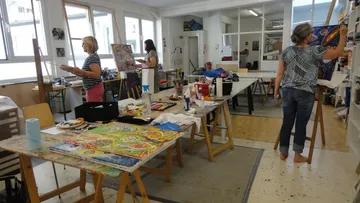 Three women paint in a creative, bright studio.