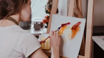 Artist paints with brush on canvas in a studio-like environment.