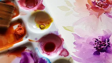 Watercolor palette with brush, floral drawing in the background.