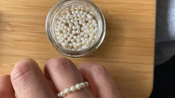 Pearl ring on hand, next to glass with other pearls.