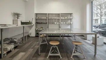 Empty room with tables, chairs, and shelves full of dishes.