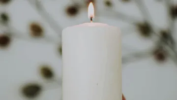 White candle burning, background with blurry leaves