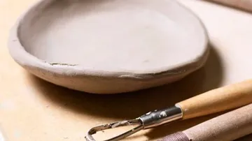 Teller aus Ton liegt auf einem Tisch, Werkzeuge daneben.