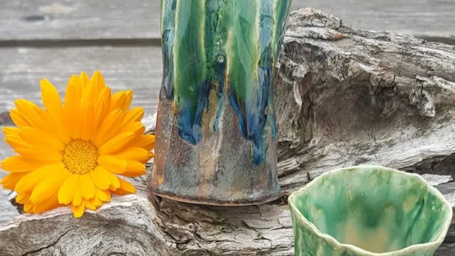 Green ceramic mugs stand on a piece of wood surrounded by a flower.