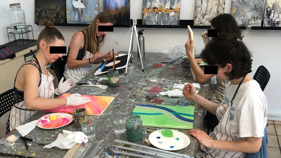 Four women painting canvases at a studio table.