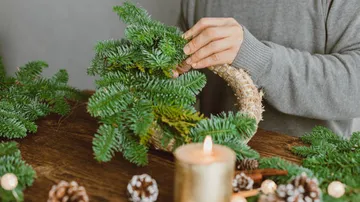 A person arranges a wreath of pine branches on a table.
