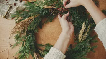 Hände dekorieren einen Kranz mit Beeren und Pflanzen.