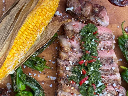 Gegrilltes Fleisch mit Salsa, umgeben von Gemüse und Mais.