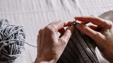 Grey wool is made into a knitted part with hands.