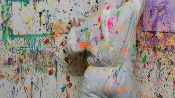 The person is wearing a jumpsuit and painting a wall.