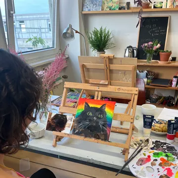 Eine Person malt ein schwarzes Katzenporträt in einem Atelier.