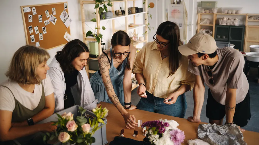 Five people look at materials on a table in a creative space.