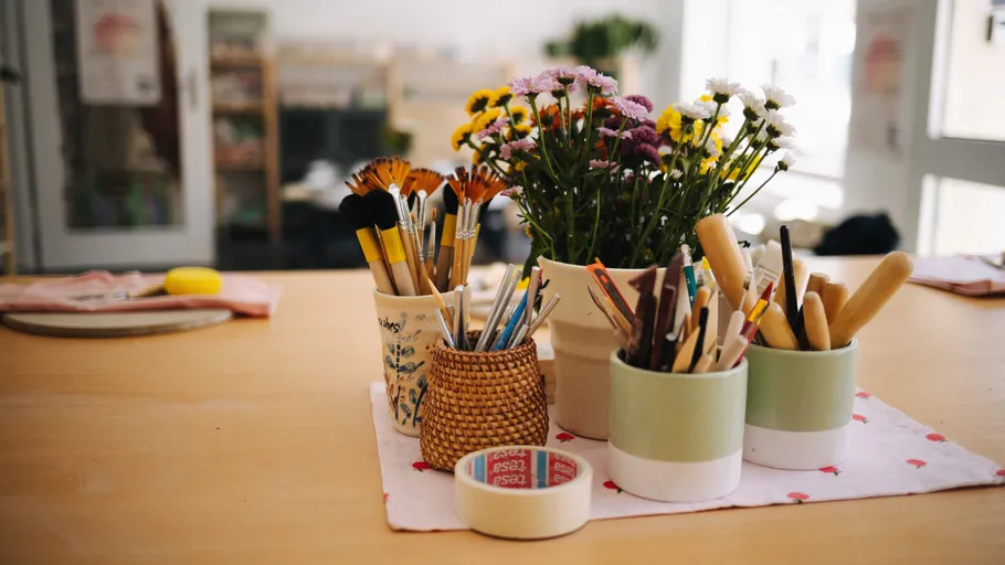 Bunte Stifte und Pinsel stehen in Töpfen auf einem Tisch.