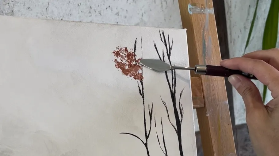 A hand paints on a canvas with a spatula.