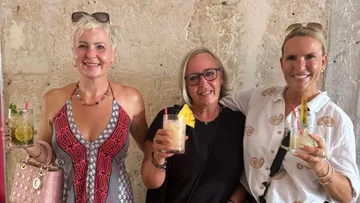 Drei Frauen halten Cocktails in einem rustikalen Ambiente.