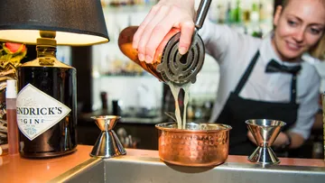 Bartender pours drink through sieve into copper cups.