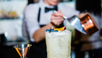 Cocktail steht bereit, Barkeeper mischt Zutaten hinter der Bar.