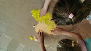 Zwei Kinder malen mit Händen auf dem Boden.
