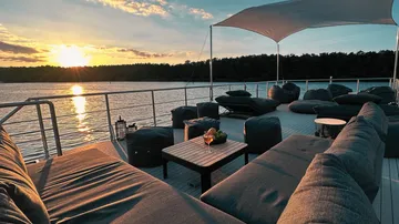 Sofa and table on terrace, sunset over water.