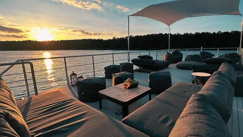 Sofa and table on terrace, sunset over water.
