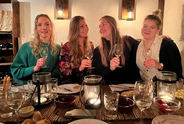 Vier Frauen stoßen mit Weingläsern an, bei Kerzenlicht.