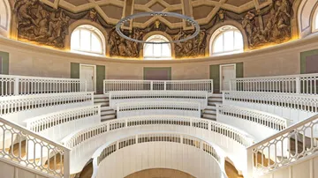Runder Saal mit weißen Bänken und großen Fenstern.