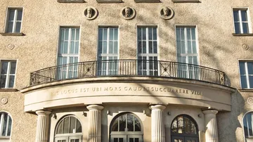 Gebäude mit Säulen, Fenstern und einem geschwungenen Balkon.