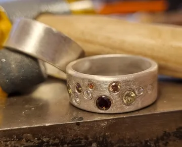 A metallic ring with colorful stones on a workbench.