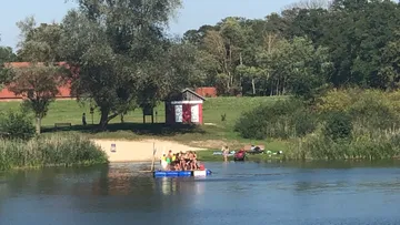 Board with children swims on a calm body of water.
