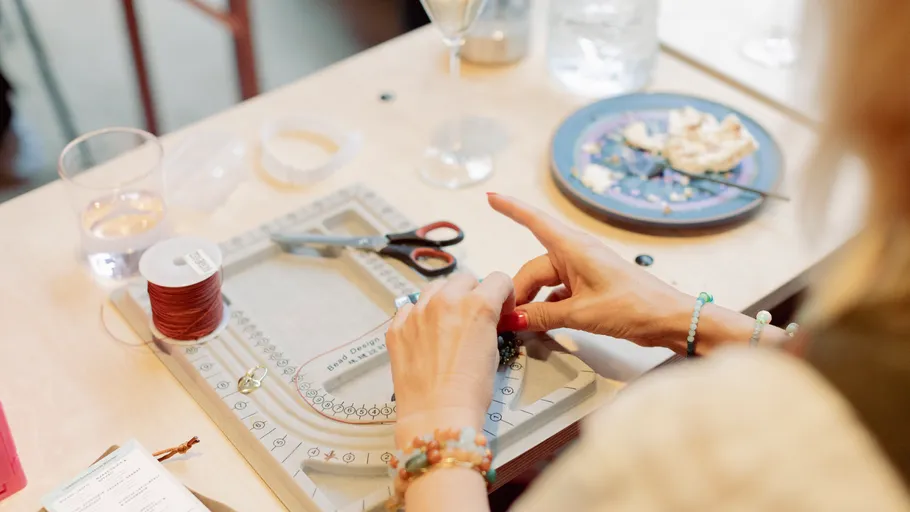 Hände gestalten Schmuck auf einem Tisch mit Materialien.