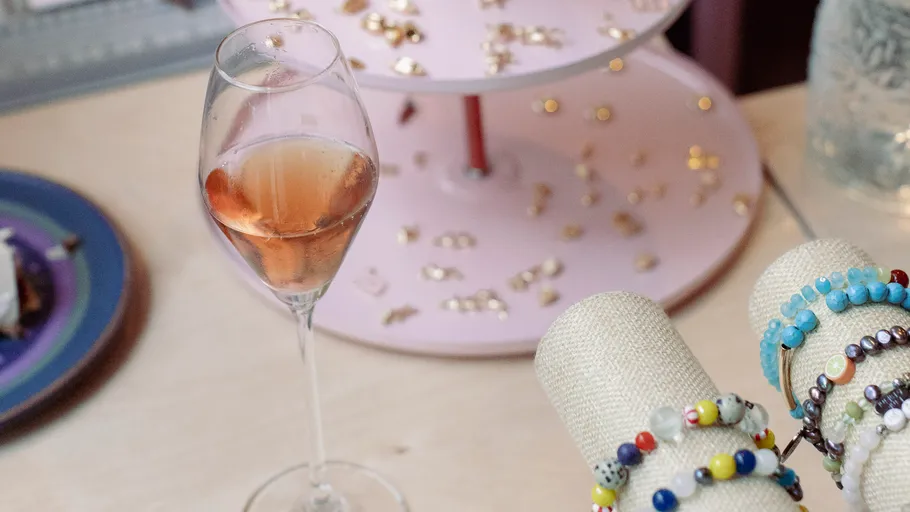 Ein Glas Roséwein steht neben Schmuck auf einem Tisch.