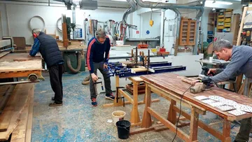 Drei Personen arbeiten an Holzprojekten in einer Werkstatt.