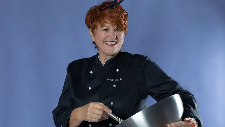 Smiling chef in black coat stirring large bowl.
