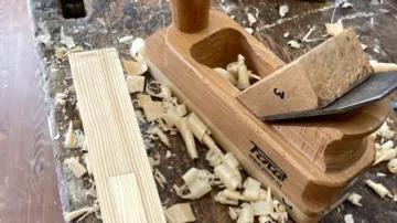Wood hand planer smoothes out pieces of wood on a workbench full of chips.