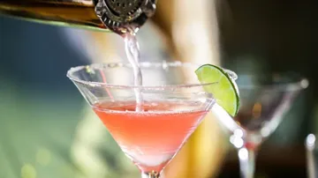 Cocktail wird in ein Glas mit Limettenscheibe gegossen.