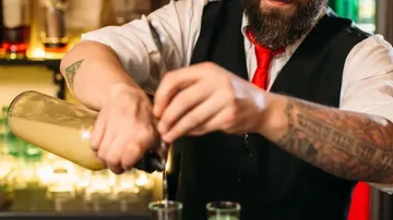 Barkeeper gießt Schnaps in Gläser, in Barumgebung.