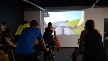 Gruppe von Personen auf Fahrrädern, vor Projektionsleinwand.