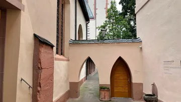 Engpass zwischen Gebäuden, Eingangstür, umgeben von Bäumen.