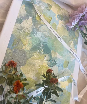 Gemälde mit pastellfarbenem Muster, umgeben von Blumen und Bändern.