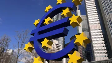 Euro symbol surrounded by yellow stars in front of modern buildings.