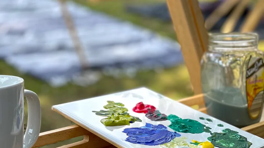 Paints on palette, beaker next to it, picturesque surroundings.