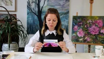 Woman holds up a picture and looks at it at the table.