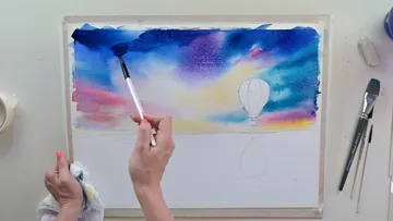 Eine Hand malt Wasserfarbe auf Papier mit Ballon.