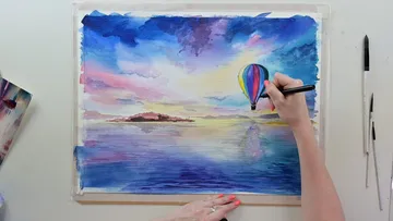 Eine Hand malt eine bunte Heißluftballon-Szene.