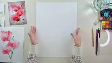 Leeres Blatt Papier, Hände zeigen nach oben, Malutensilien liegen daneben.