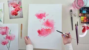 A person paints pink flowers on white paper.