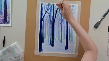 A hand paints trees on a piece of paper.