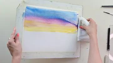 Händed halten ein angefeuchtetes Tuch über ein Aquarell.